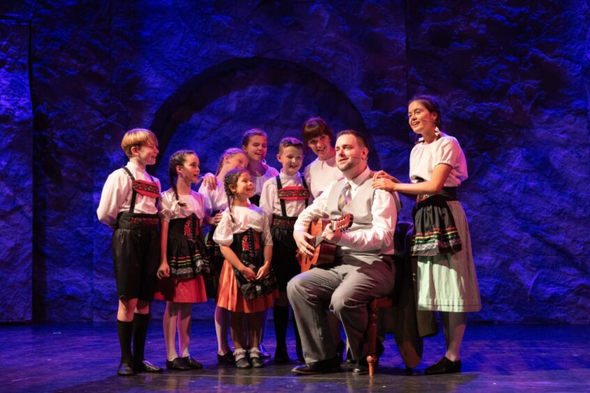 Scene from The Sound of Music at Eden Court, Inverness: Liam Macaskill as Captain Von Trapp seated, playing the guitar with his seven children singing with him. 