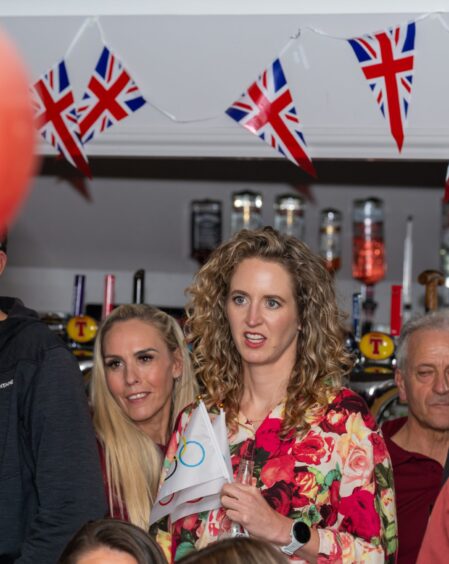 Two women standing below bunting and waving Olympic flags.