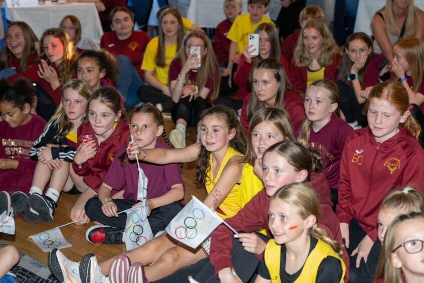 Youngsters dressed in Maroon and yellow cheering on Megan Keith at the Olympics.