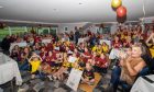 Crowds cheering at a watch party in Inverness with a maroon and gold/ yellow colour scheme.