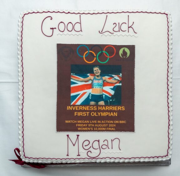 A square white cake with Good luck Megan on the front, the olympic rings and a picture of Megan holding a union jack flag.