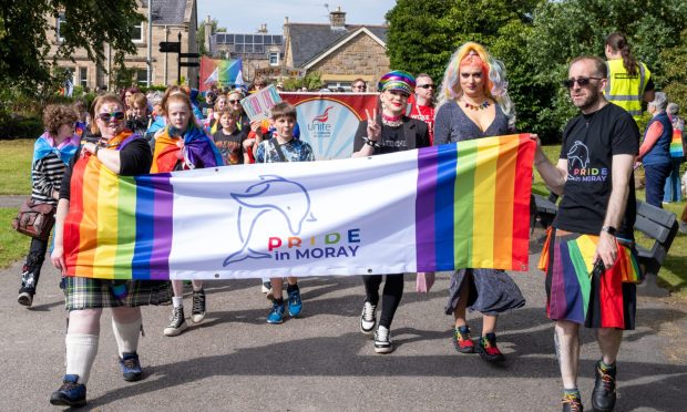 Pride in Moray parade marching behind rainbow banner.