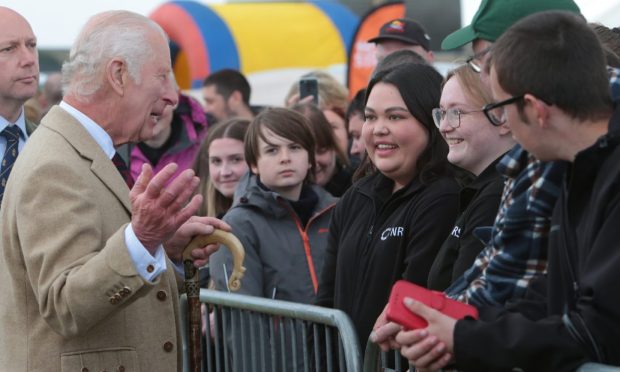 King Charles meeting spectators in the rain behind a metal fence.