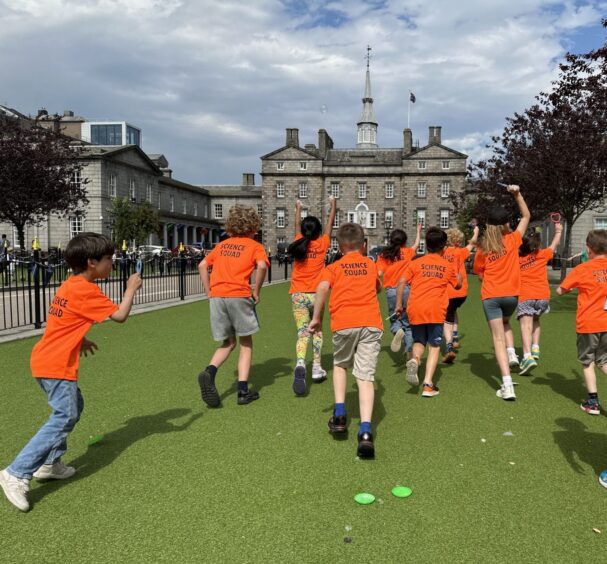 Children in orange running across grass