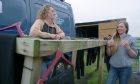 . Iona McLachlan and her boyfriend Finn MacDonald of North Coast Watersports in front of their van leaving against a fence.