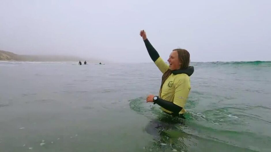 Iona standing in the water with her arm in the air in celebration.