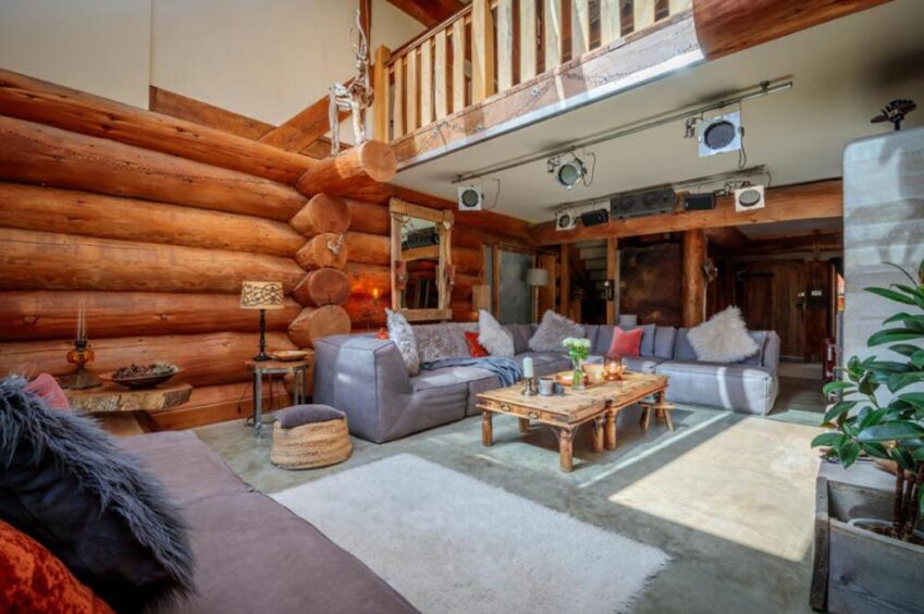 Lounge with grey settee and wooden log walls.