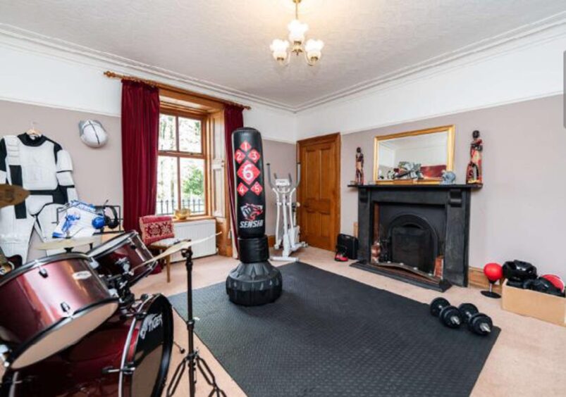 Large room with black fireplace, sash windows, drum kit and punching bag. 