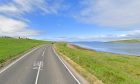 general view of blue skies and small beach on the right of the windy road surrounded by fields.