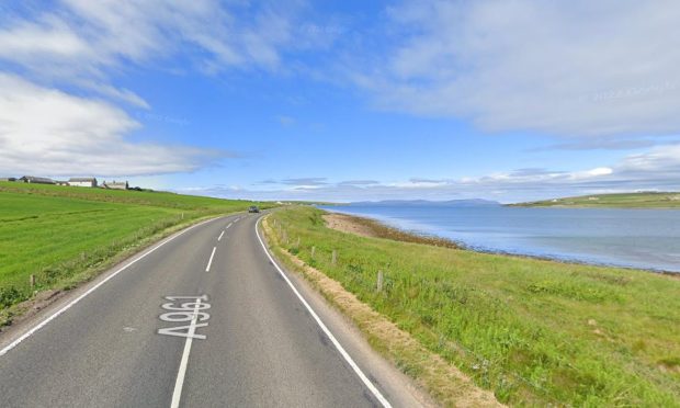 general view of blue skies and small beach on the right of the windy road surrounded by fields.