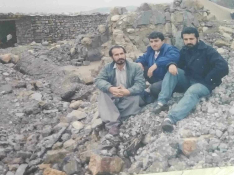 Soran (right) sitting outside what was left of his childhood home in Khurmal after it was destroyed by troops with his older brother and cousin.