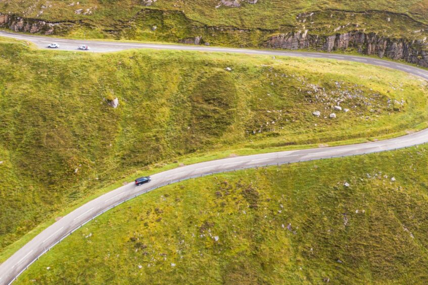 three cars seen from above on a winding road in the Quinag Mountain Range in the Highlands. 