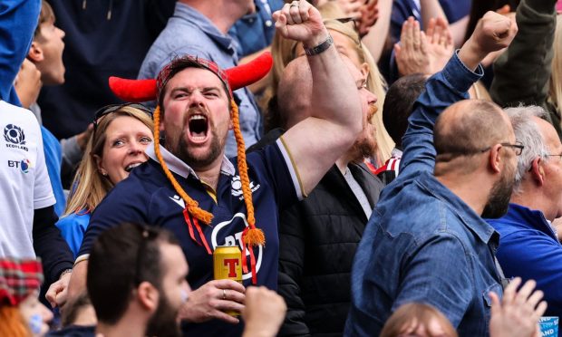 A Scotland rugby fan enjoys a game at Murrayfield while drinking a beer. Image: Shutterstock.