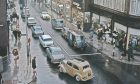 This colourisation of a busy scene in Aberdeen's St Nicholas Street on a dreich day in 1965 almost looks like the cover from a Ladybird book. Reid and Pearson's department store on the corner of St Nicholas Street and Schoolhill was celebrating its 25th anniversary. Image: DC Thomson.