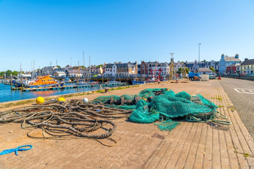 Stornoway, Scotland - August 16 2023: A fishing net and rope lies along the docks at the fishing pier, with the Scottish town of Stornoway behind on Lewis and Harris Island, Stornoway, Scotland.