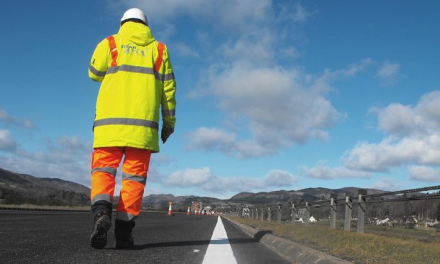 Bear Scotland worker in florescent jacket and orange trousers walking along white line at the side of the road.