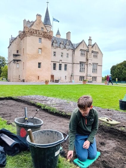 Boy kneels down and prepares to dig in a patch of land in front of Brodie Castle