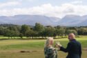 couple shares a toast against a sweeping view of the Scottish Highlands