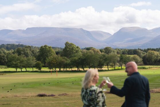 couple shares a toast against a sweeping view of the Scottish Highlands