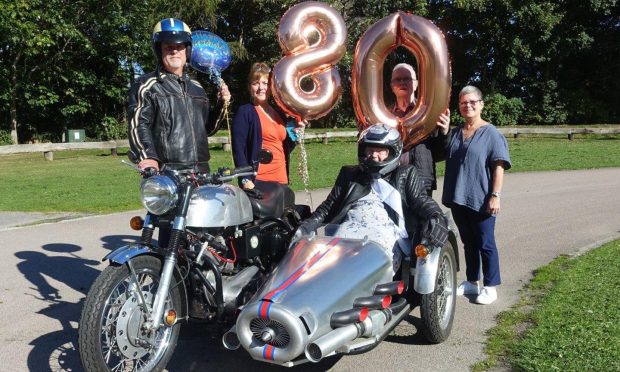 Irene with her family around the motorcycle with 80 birthday balloons in the background.