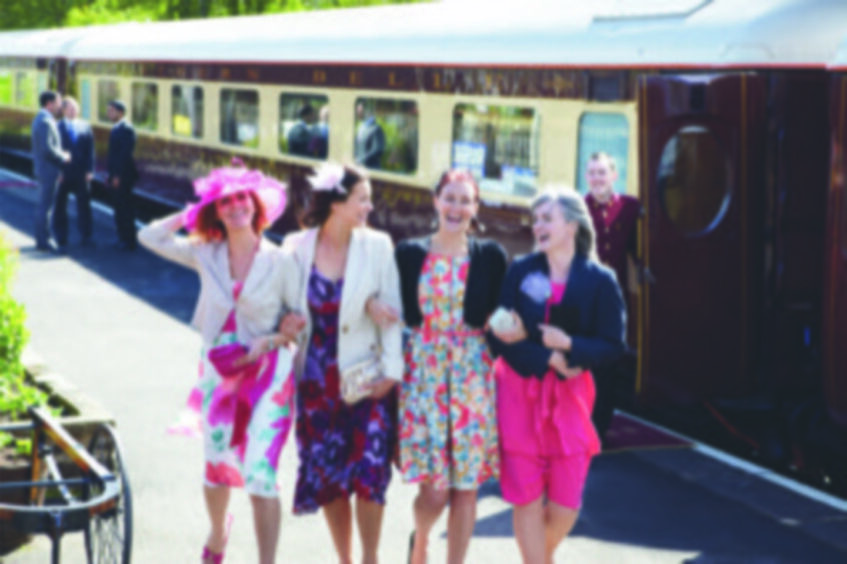 Women dressed in dresses and hats standing in front of Northern Belle train carriage.