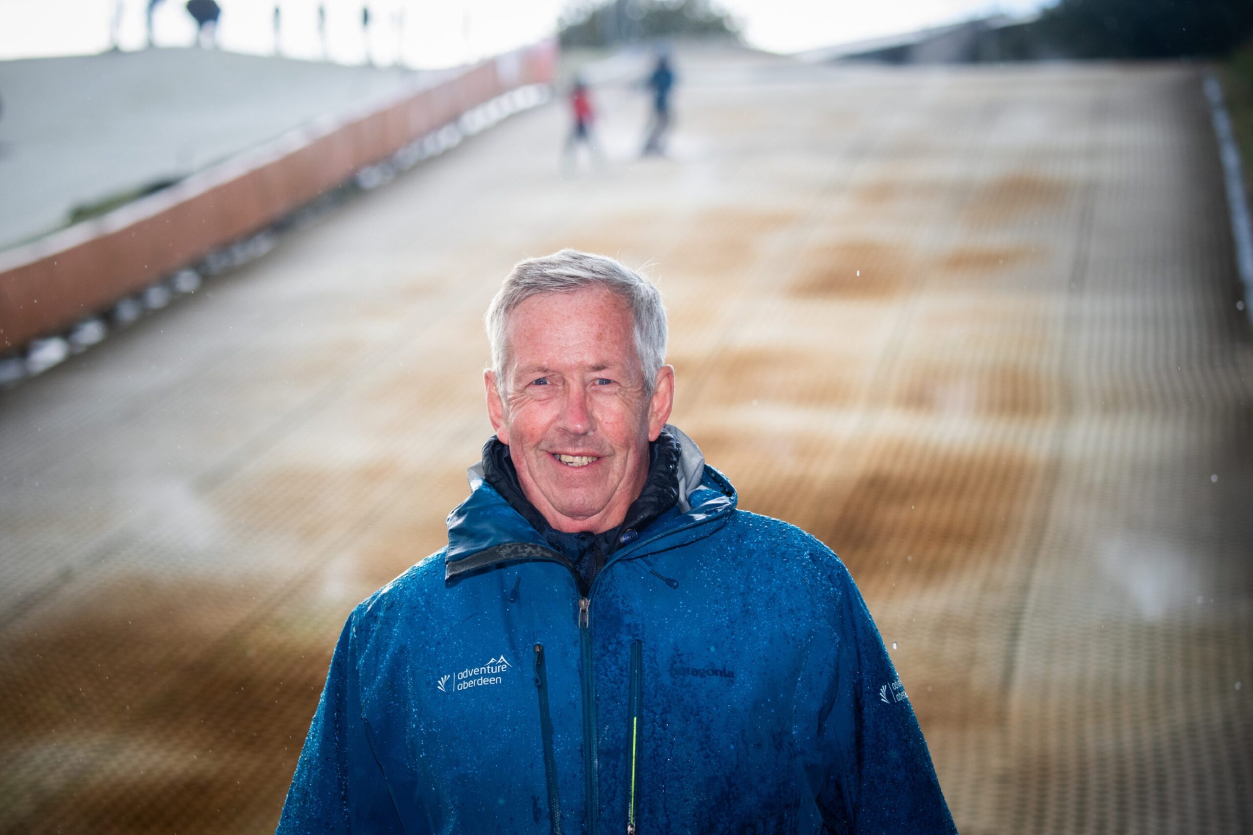 Bob Thow smiling at the camera with Garthdee ski slope behind him in Aberdeen 