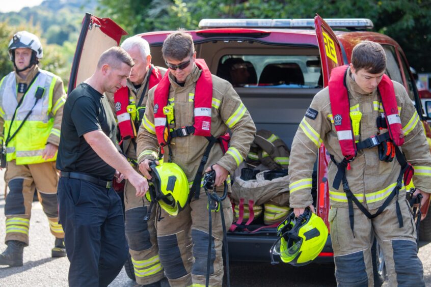 Firefighters gearing up in front of a red van with the back doors open.