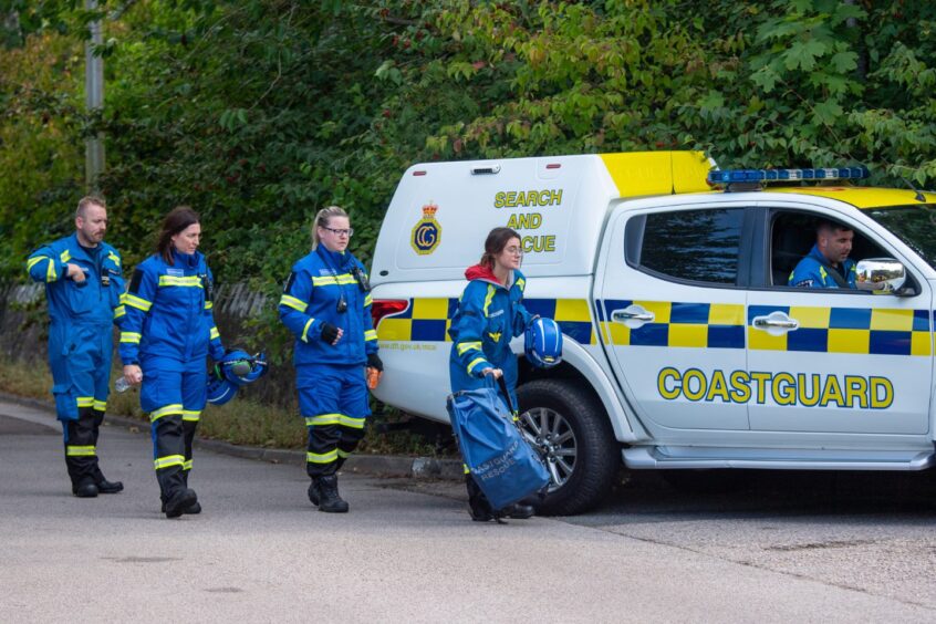 Coastguard teams in blue walking by company vehicle.