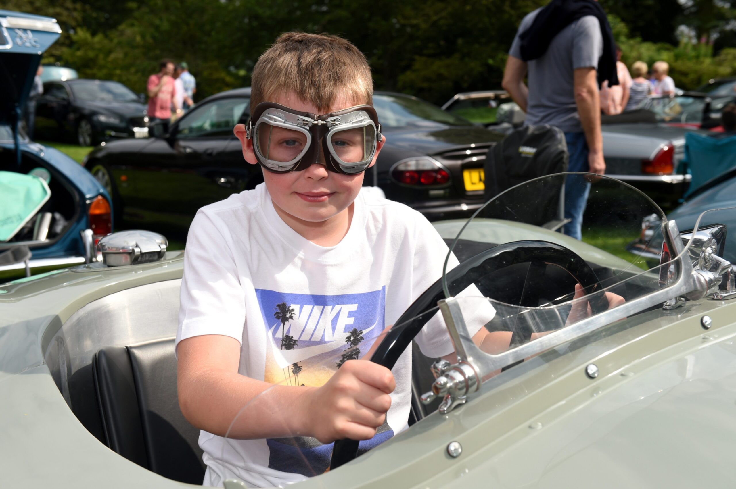 Callum as a ten year old wearing racing goggles, behind the wheel of a stationary Jaguar C-type 1954.