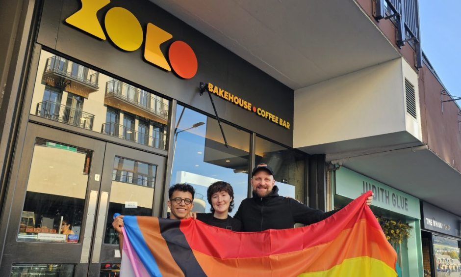 Fernando Basaldua Bazaldua, Ro O hEadhra and Tristan Aitchison holding a pride flag outside XOKO cafe in Inverness.