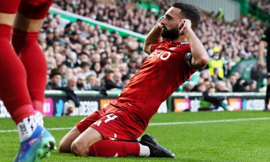 Aberdeen captain Graeme Shinnie slides on his knees, holding his fingers to his ears, in celebration of scoring in the 2-2 draw against Celtic at Parkhead.