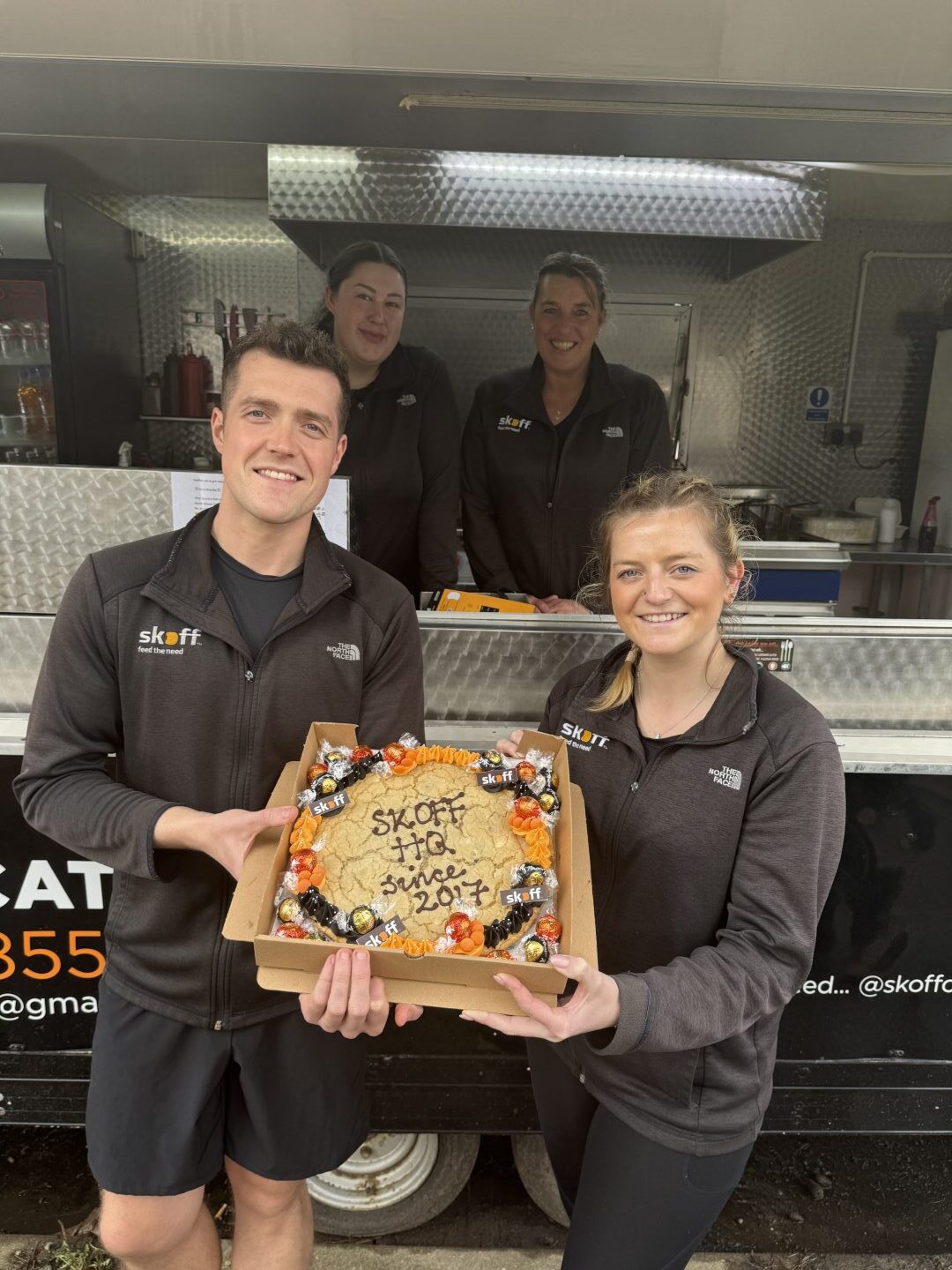 The family holding a desert with chocolate lettering reading 'Skoff HQ since 2017'