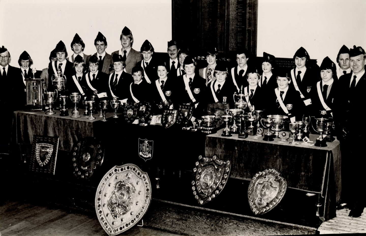 Image shows members of the boys' brigade, in full uniform, standing behind a table that is filled with awards in 1980