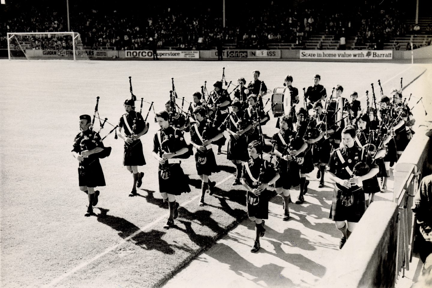 Image shows the Boys' Brigade pipe band walking around the perimeter of the football pitch at Pittodrie