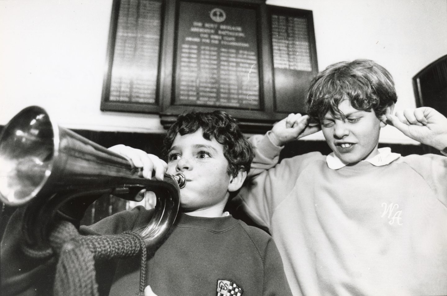 Image shows one member of the band playing a trumpet, whilst another child is covering his ears