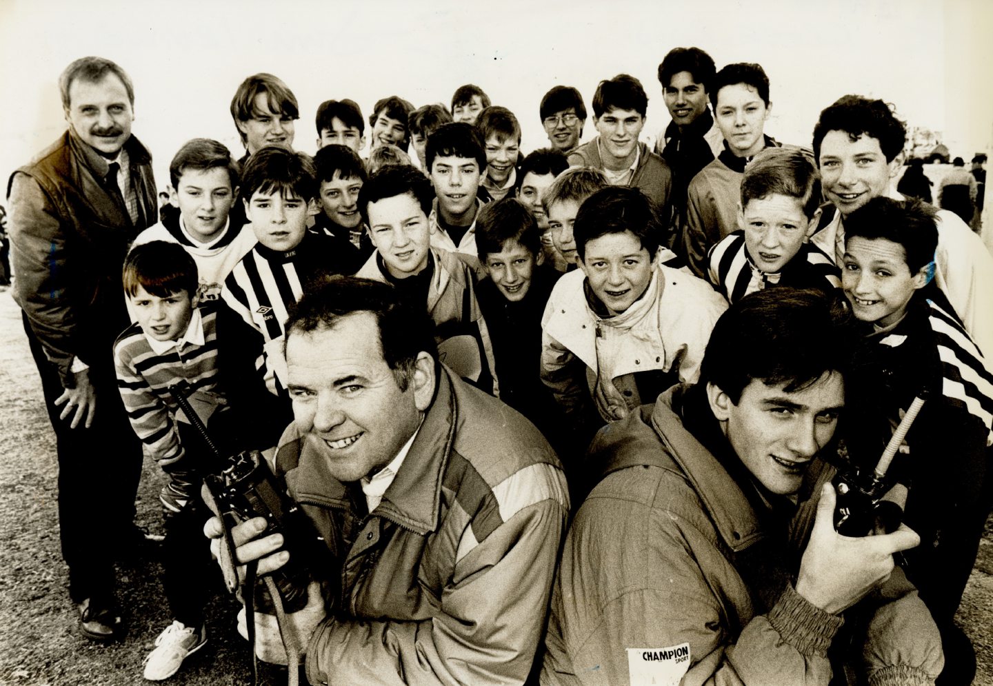 A group of Boys' Brigade boys stand together on a field with two radios, in rehearsal for a cross country running race.