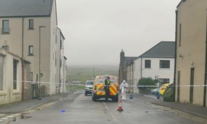 Forensic officer next to police car and officer behind police tape on a street in Orkney.