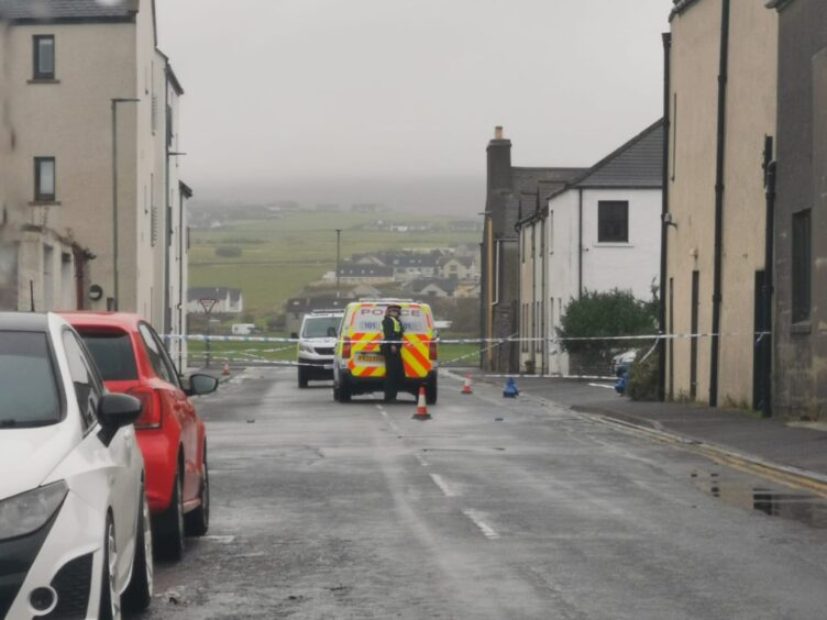 Police car and officer behind police tape on Kirkwall street