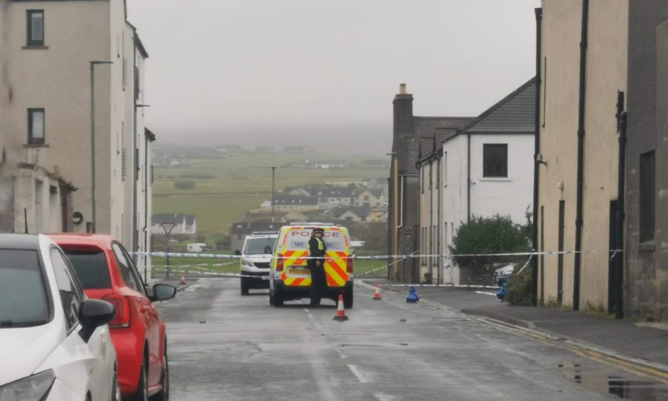 Police car and officer behind police tape on Kirkwall street