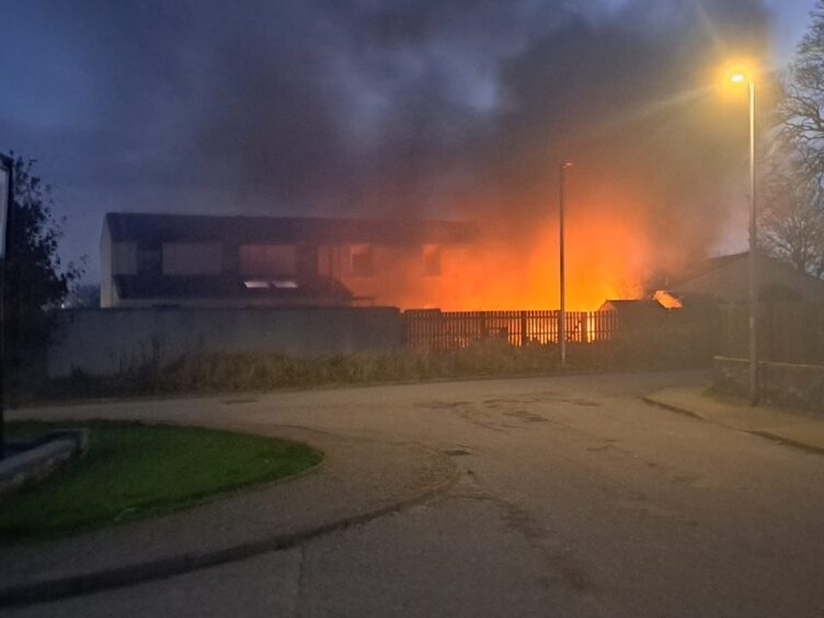 Property illuminated in orange as smoke rises from a fire in the back garden of a residential house.,