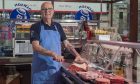 Michael Dawson behind butcher counter chopping meat.