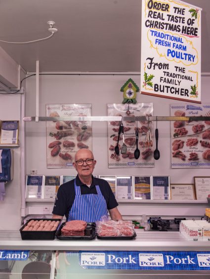 Michael Dawson behind butcher counter with Christmas sign above. 