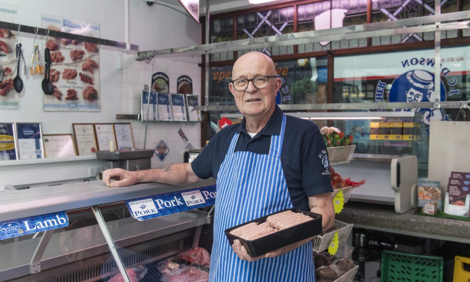 Michael Dawson holding plate of sausages at counter. 