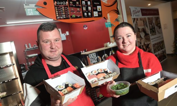 Kamil Luczak with his partner Aldona Fryc of Sushi Inverness dressed in red aprons and holding food boxes filled with sushi.