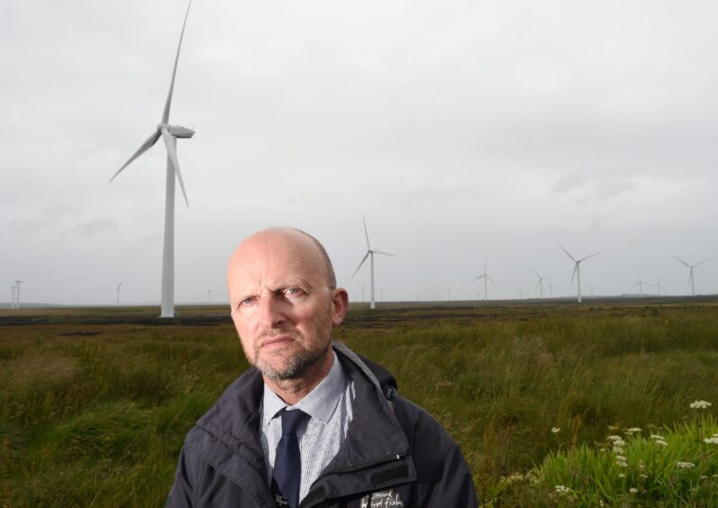 Highland Councillor Matthew Reiss with a wind farm behind him