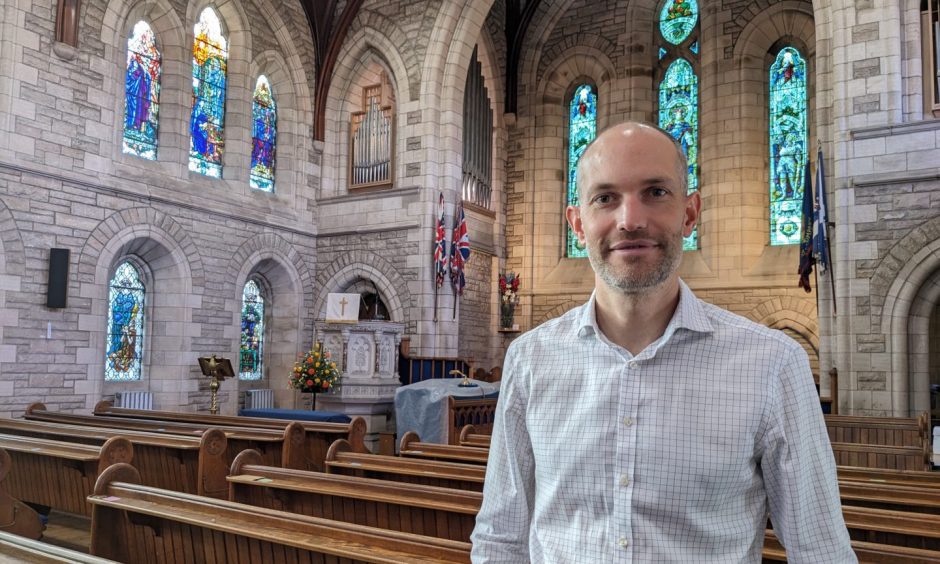 Edward Fitsell standing in St Laurence Church with stained glass windows behind. 