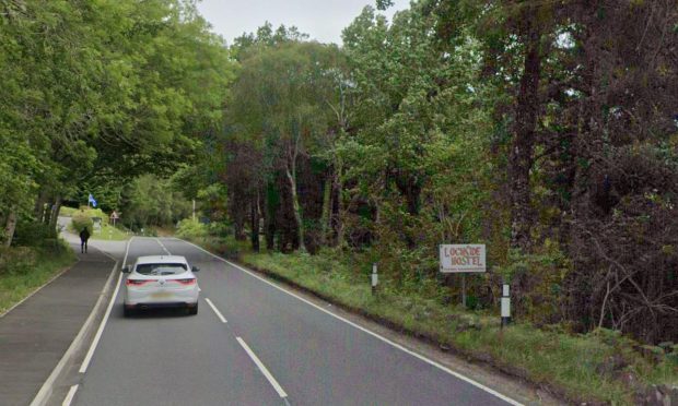 White car travelling on A82 with trees on each side.