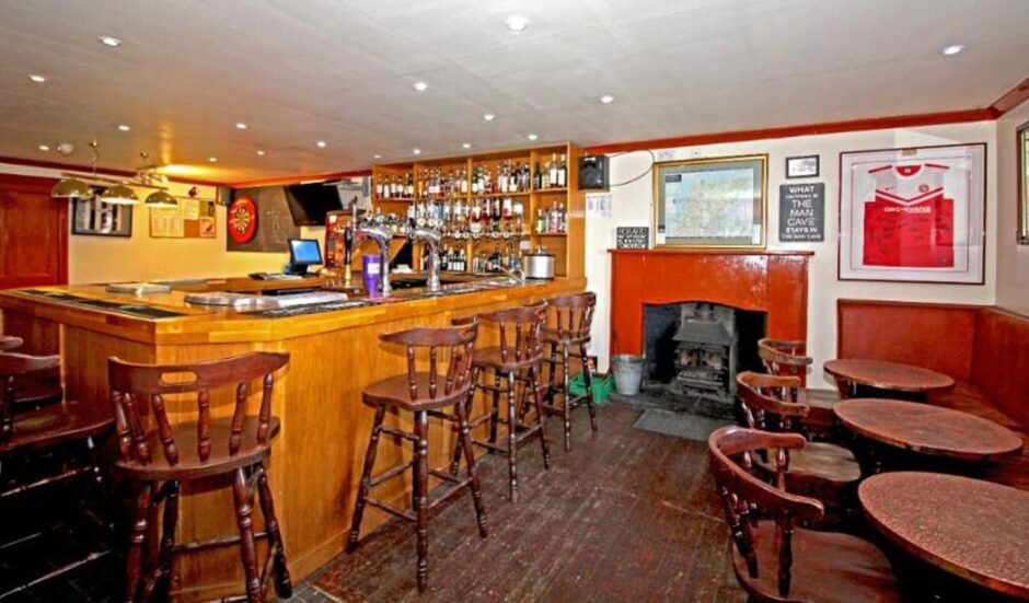 View of wooden bar with bar stools, fireplace and dart board.