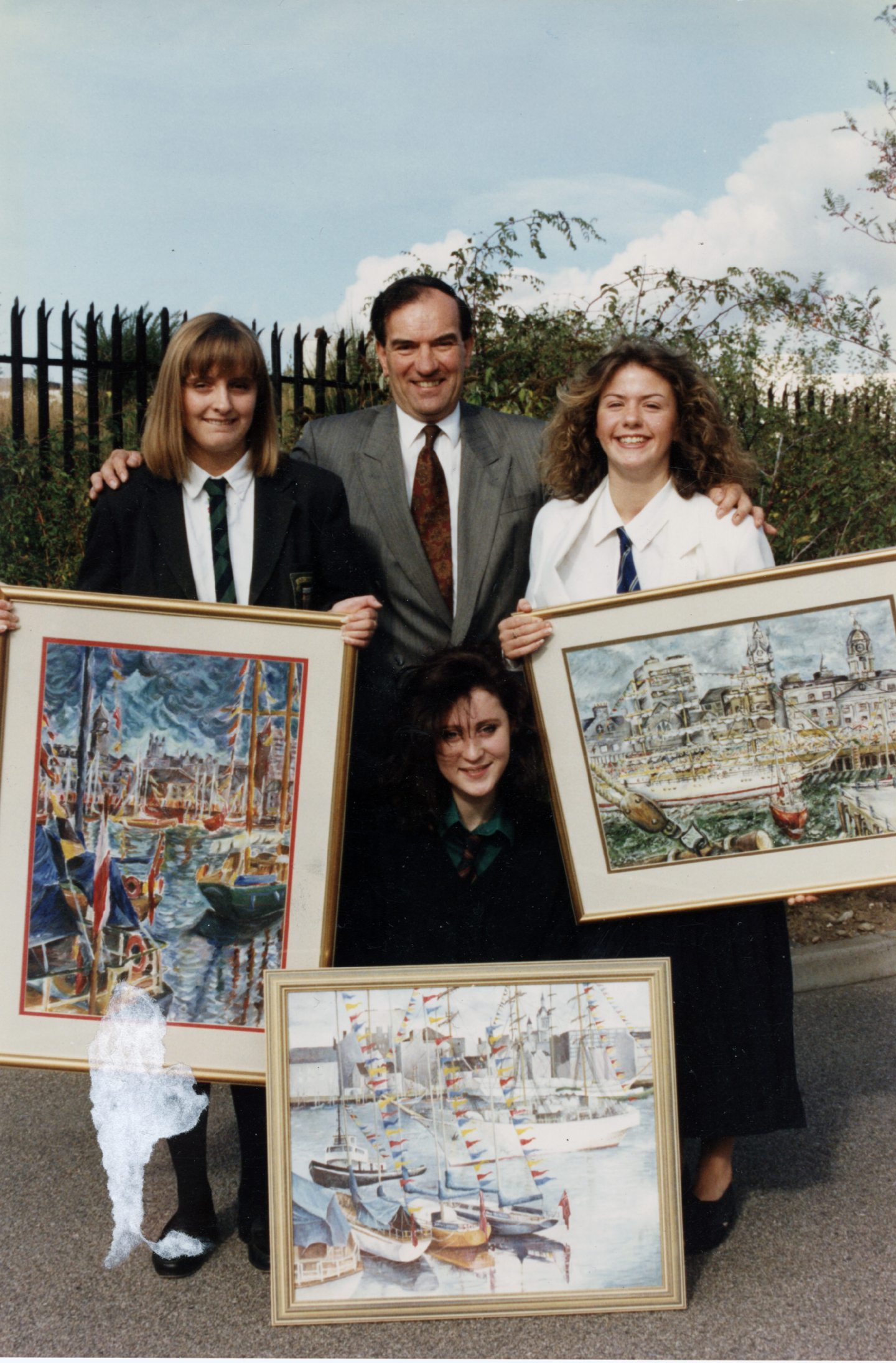 Three women presenting paintings of the tall ships race with a man behind them