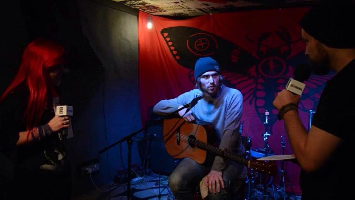 Craig John Davidson sitting down with a guitar during an interview.